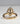 A gold ring with a large oval clear gemstone pavé-set on top of a polished gold band, photographed on a neutral light gray background.