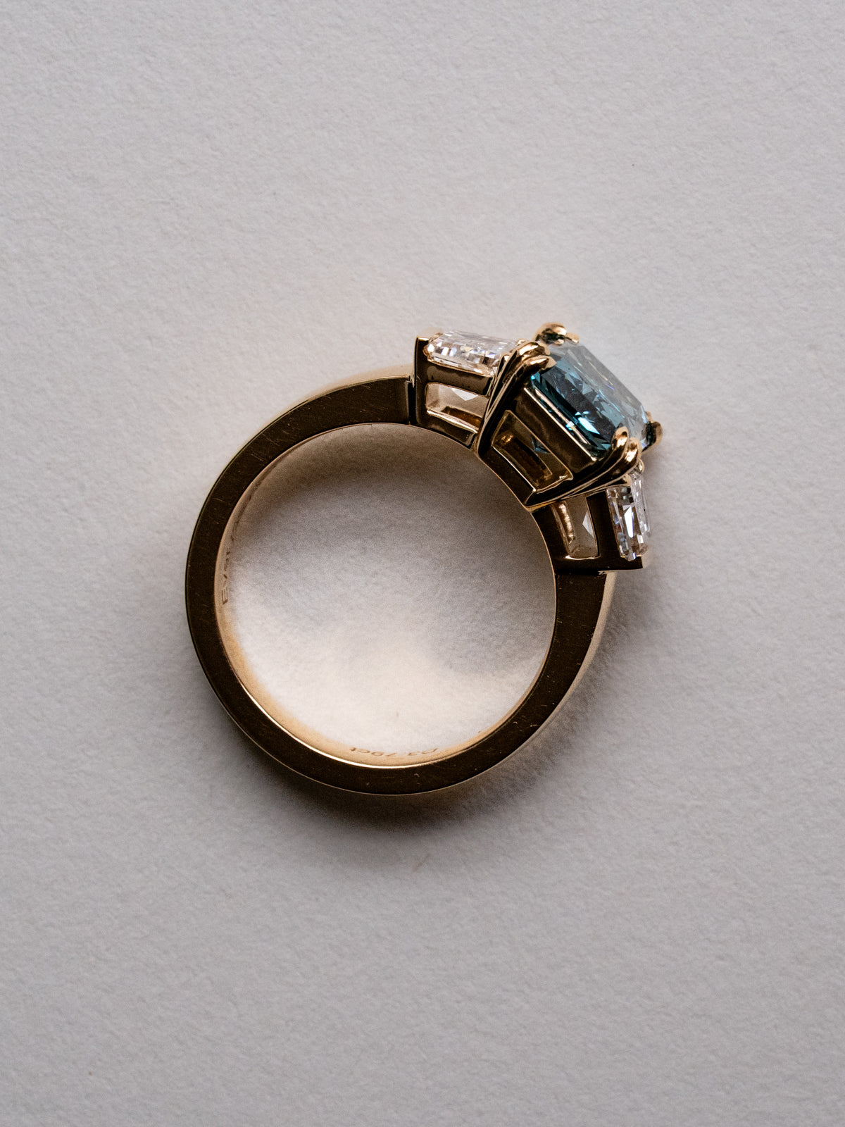 Side profile of a blue radiant cut three-stone engagement ring in yellow gold with step-cut trapezoid diamonds