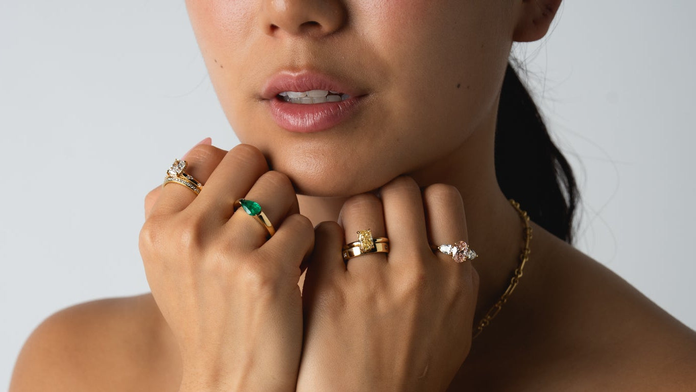 Woman wearing multiple rings and bracelets on a plain background